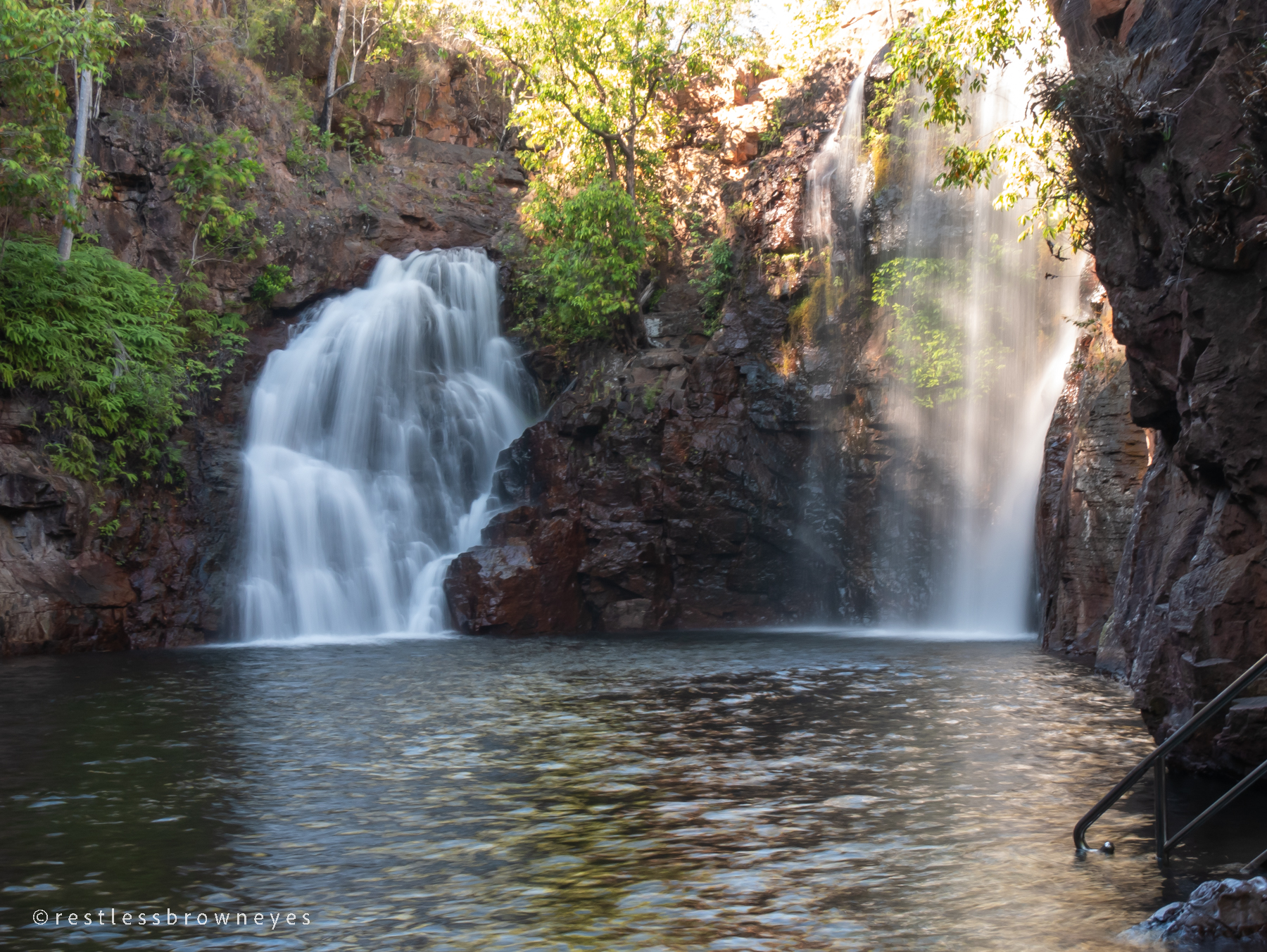 two waterfalls falling into a pool of water with a backdrop of a rocky gorge