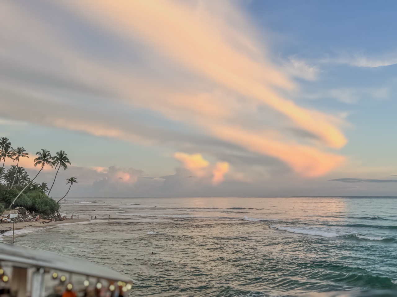 Palm trees on the left encircle calm waters, the roof of restaurant with festoon lights frames the lower left corner